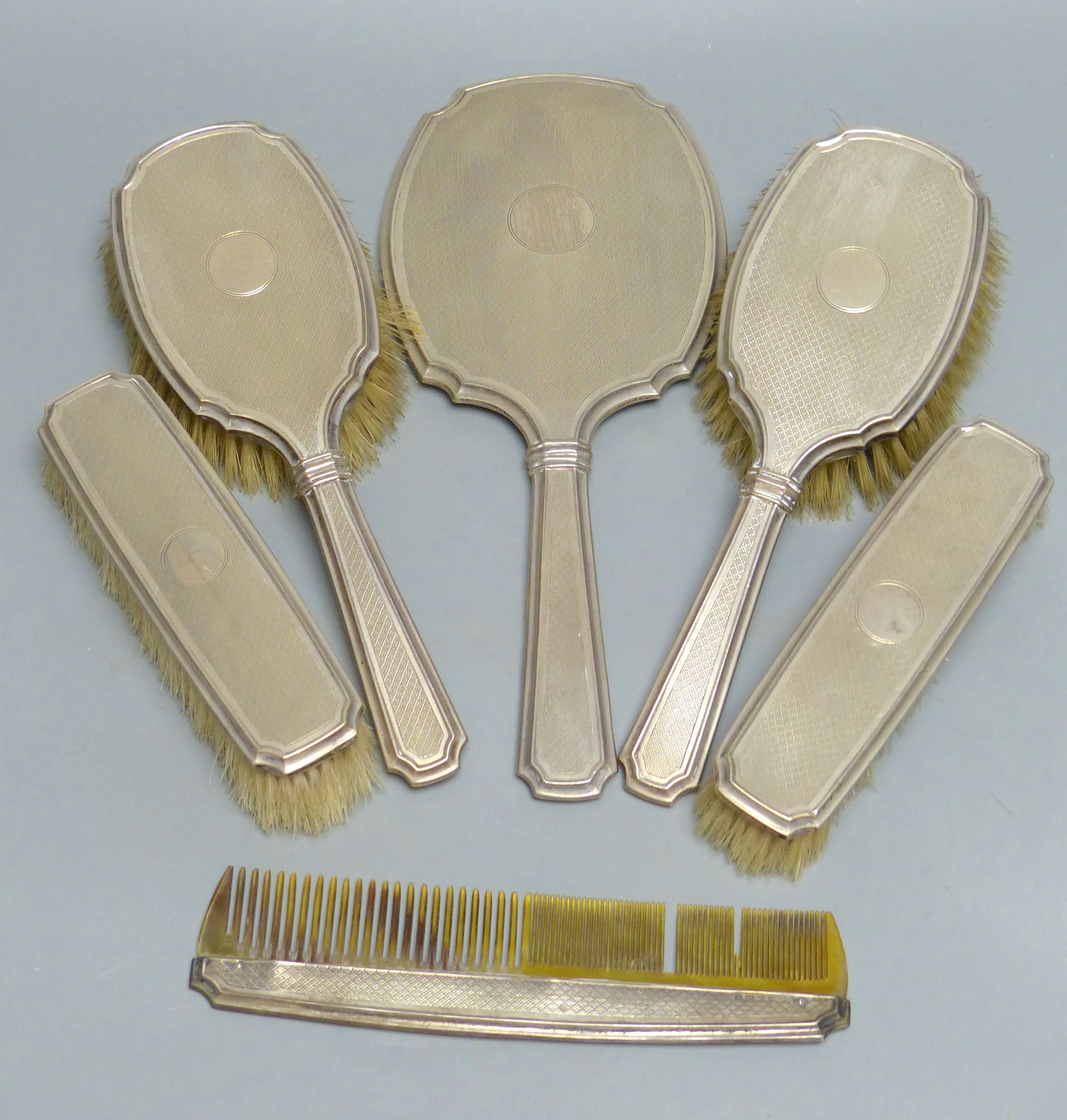 A six-piece engine-turned silver-mounted dressing table set, comprising two pairs of brushes, a comb and a hand mirror, Birmingham 1929